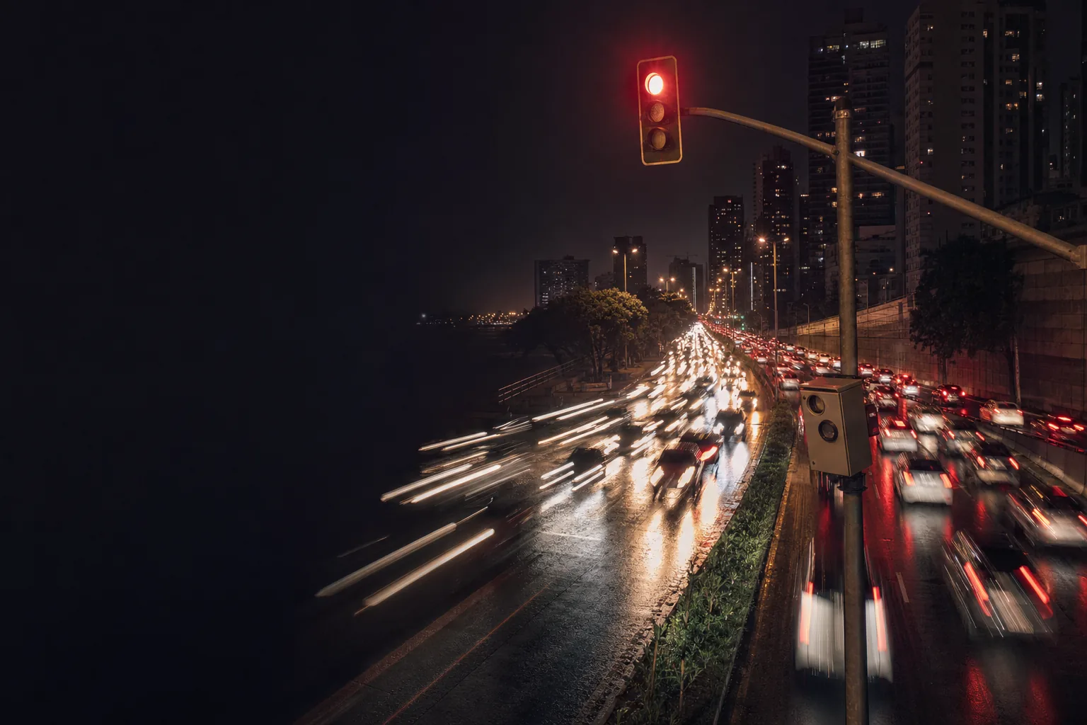 Avenida à noite com semáforo vermelho e radar de velocidade